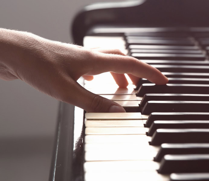 Hand playing the piano, white keys, black keys, surrounded by soft, warm light.